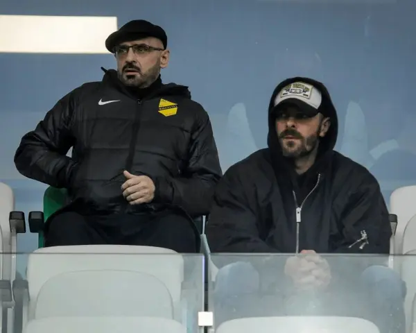 Właściciel wieczystej kraków, w czapce i okularach, siedzi obok mężczyzny w bluzie z kapturem.