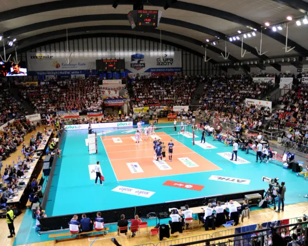 Widownia kibicuje podczas meczu siatkówki ZAKSA. Pełna hala, zawodnicy na boisku, emocje sięgają zenitu.