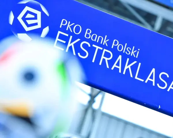 Niebieska tablica z logo PKO Bank Polski i napisem EKSTRAKLASA. W tle piłka nożna, gdy terminarz ekstraklasy.