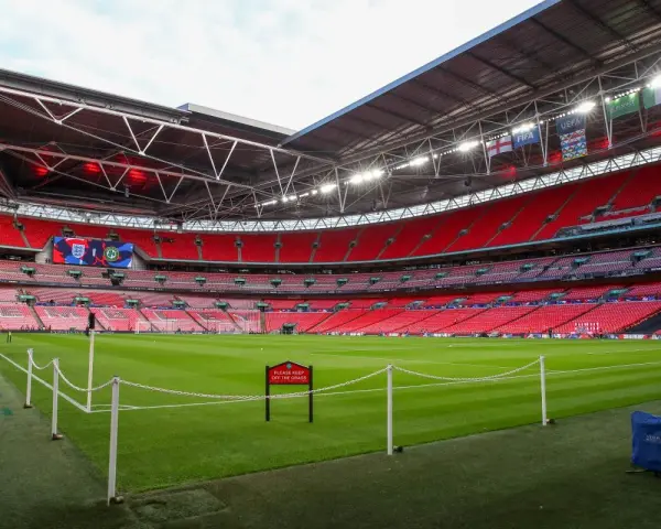 Pusta, czerwona trybuna stadionu Wembley, największego stadionu na świecie, z zieloną murawą i tabliczką "Prosimy nie wchodzić na trawę".