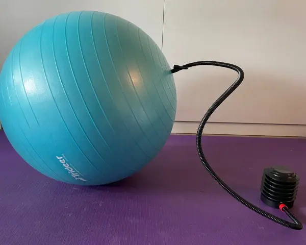 Niebieska piłka fitness podłączona do pompki na fioletowej macie.