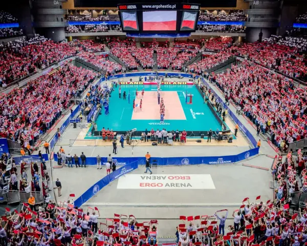 Widownia Ergo Areny, wypełniona kibicami z flagami Polski, dopingująca mecz siatkówki. Ogromna pojemność hali robi wrażenie.