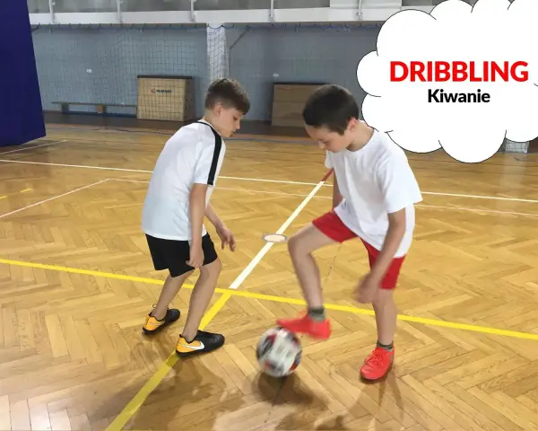 Dwóch chłopców ćwiczy drybling piłką nożną na sali gimnastycznej.