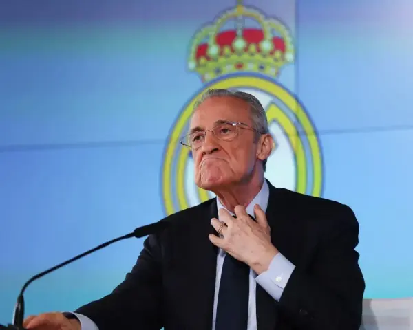 Florentino Pérez, prezes Realu Madryt, w garniturze, z ręką na szyi, na tle logo klubu.