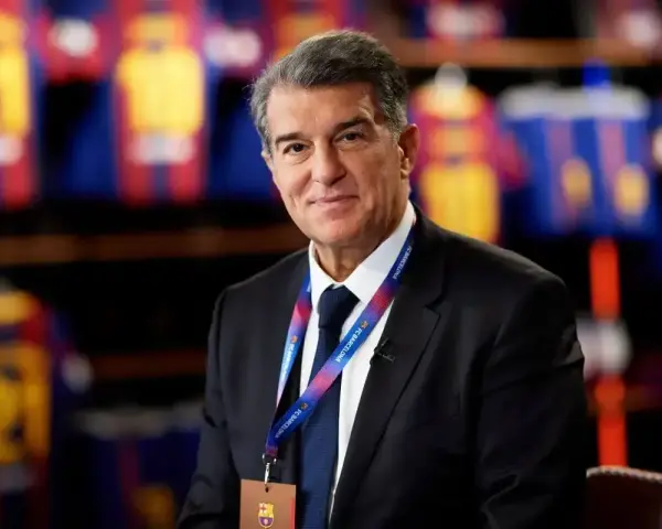Uśmiechnięty prezes Barcelony, Joan Laporta, w garniturze, z identyfikatorem FC Barcelona na szyi.