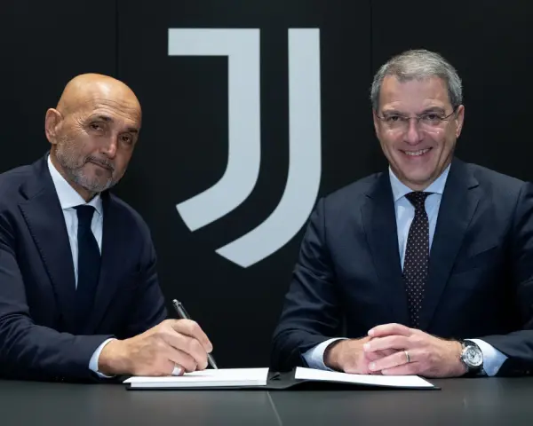Dwóch mężczyzn w garniturach siedzi przy stole. Jeden z nich, łysy, podpisuje dokument. Za nimi logo Juventusu.