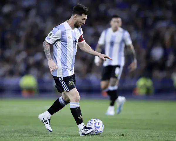 Lionel Messi w koszulce Argentyny prowadzi piłkę, gotowy do zdobycia kolejnych bramek. Fani zastanawiają się, ile goli ma Messi.