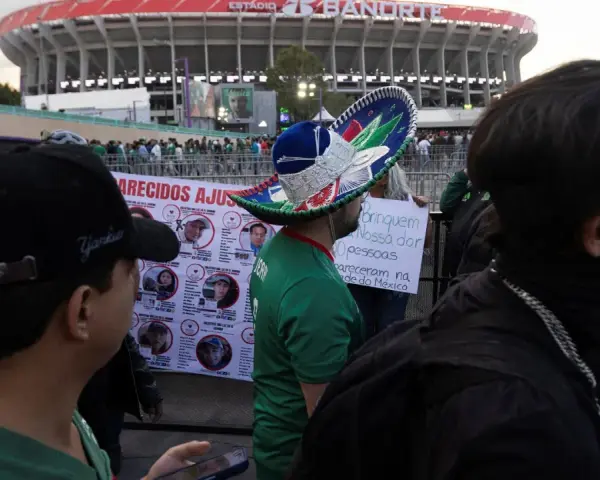 Tłum ludzi przed stadionem Azteca. Na pierwszym planie mężczyzna w meksykańskim kapeluszu, obok baner z portretami zaginionych.
