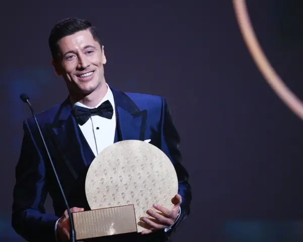 Uśmiechnięty Robert Lewandowski w eleganckim garniturze odbiera nagrodę, być może Złotą Piłkę.