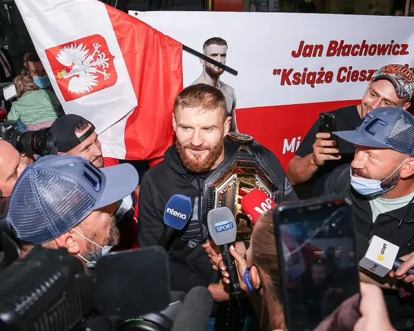 Jan Błachowicz, "Książę Cieszyński", mistrz UFC, otoczony przez fanów i dziennikarzy z polską flagą. Polacy w UFC świętują sukces.
