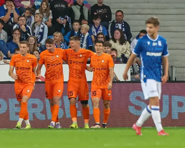 Piłkarze Zagłębia Lubin w pomarańczowych strojach świętują bramkę, podczas gdy zawodnik Lecha Poznań w niebieskim oddala się.