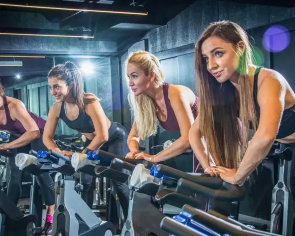 Cztery kobiety ćwiczą na rowerach stacjonarnych. Ile powinien trwać trening cardio? To zależy od celów, ale często 30-60 minut to dobry punkt wyjścia.
