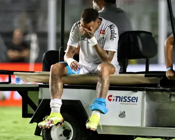 Neymar siedzi na wózku golfowym, zakrywając twarz dłońmi. Jego kontuzja jest widoczna, a zawodnik wygląda na zrozpaczonego.