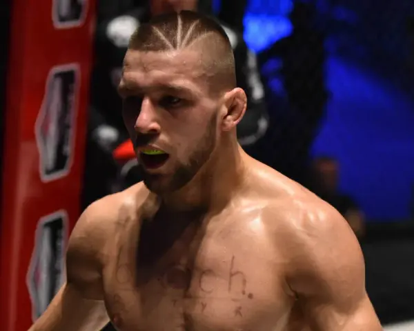 Zacięty zawodnik MMA z charakterystyczną fryzurą i ochraniaczem na zęby, gotowy do walki.