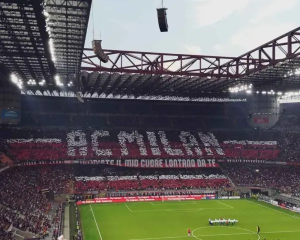 Trybuna stadionu San Siro w Mediolanie wypełniona kibicami AC Milan, tworzącymi napis "AC MILAN" i transparent "FOSSI DEI LEONI, VECCHIESTE IL MIO CUORE LONTANO DA TE".