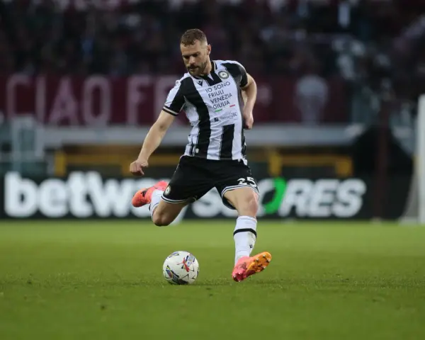 Piłkarz Jesper Karlström w czarno-białej koszulce Udinese Calcio kopie piłkę na zielonej murawie stadionu.