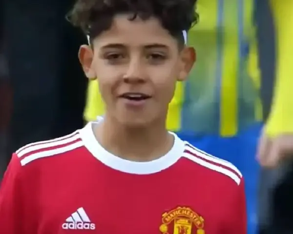 Młody piłkarz w czerwonej koszulce Manchester United, przypominający syna Cristiano Ronaldo. Jego wiek sugeruje, że to początki kariery.