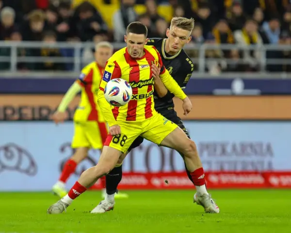 Piłkarz w żółto-czerwonej koszulce walczy o piłkę z rywalem w czarnym stroju. Intensywny przebieg: Pogoń Szczecin – Korona Kielce.