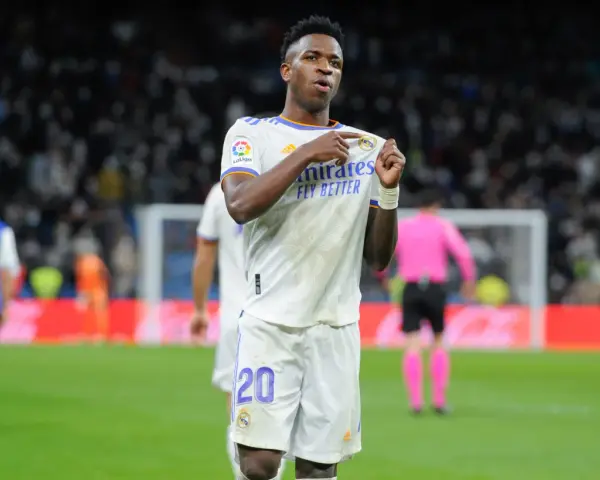 Vinicius Jr. w białej koszulce Realu Madryt z numerem 20, świętuje bramkę na tle trybun.