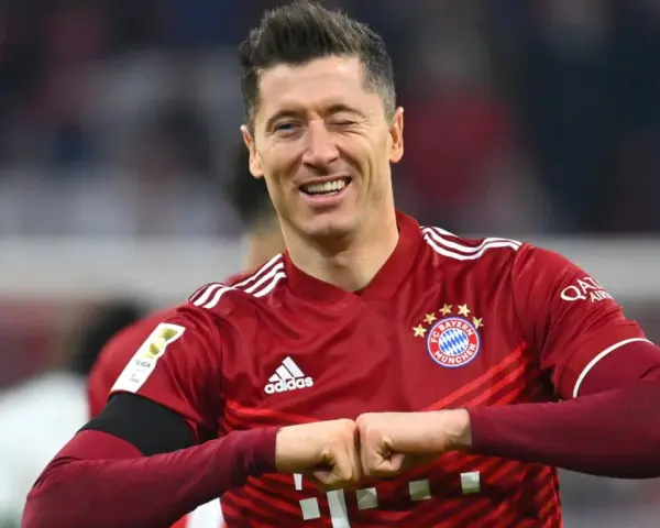 Piłkarz Robert Lewandowski w czerwonej koszulce Bayernu Monachium, uśmiecha się i zaciska pięści.