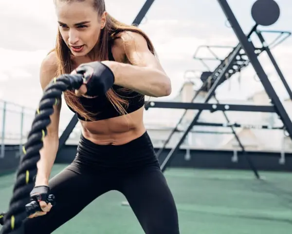 Kobieta wykonuje trening obwodowy z linami battle rope. Intensywny wysiłek buduje siłę i wytrzymałość.