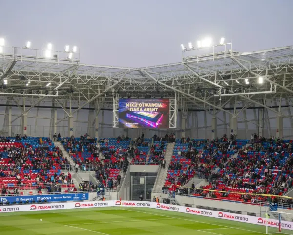 Widownia na stadionie Odra Opole podczas meczu otwarcia. Kolorowe trybuny i wielki ekran z napisem "Mecz otwarcia Itaka Areny".