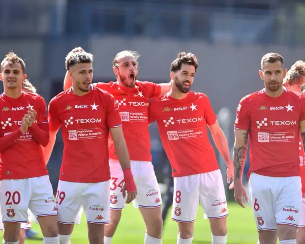 Piłkarze Wisły Kraków w czerwonych strojach, z numerami na koszulkach i spodenkach, świętują. W tle trybuny. #wisla #krakow #transfery