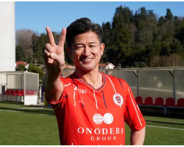 Uśmiechnięty Kazuyoshi Miura, najstarszy piłkarz na świecie, pokazuje znak pokoju na boisku.