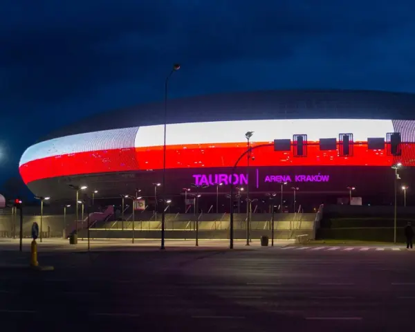 Tauron Arena Kraków nocą, z podświetloną fasadą w barwach narodowych. Obiekt mieści 15 tysięcy widzów, co czyni go jednym z największych w Polsce.