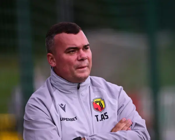 Trener Jagiellonii, z rękami skrzyżowanymi na piersi, w szarej kurtce z herbem klubu.