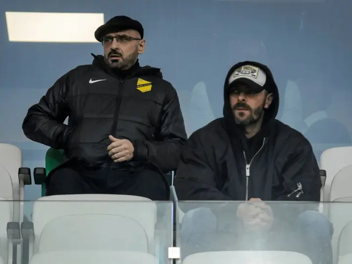 Właściciel wieczystej kraków, w czapce i okularach, siedzi obok mężczyzny w bluzie z kapturem.