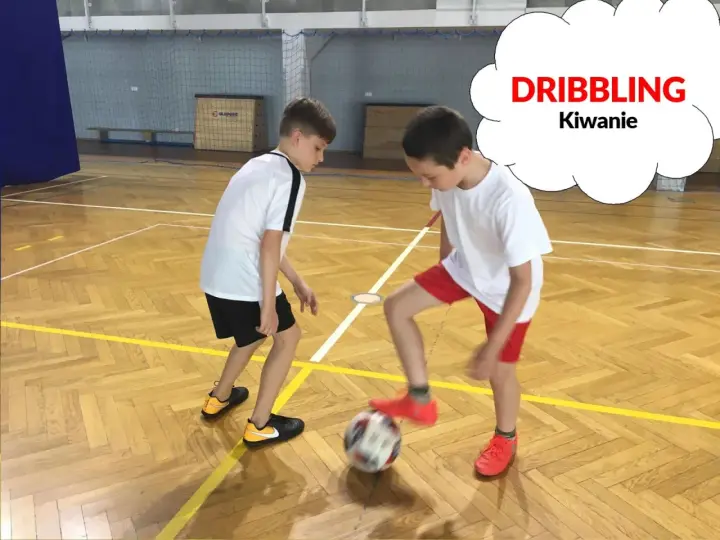 Dwóch chłopców ćwiczy drybling piłką nożną na sali gimnastycznej.