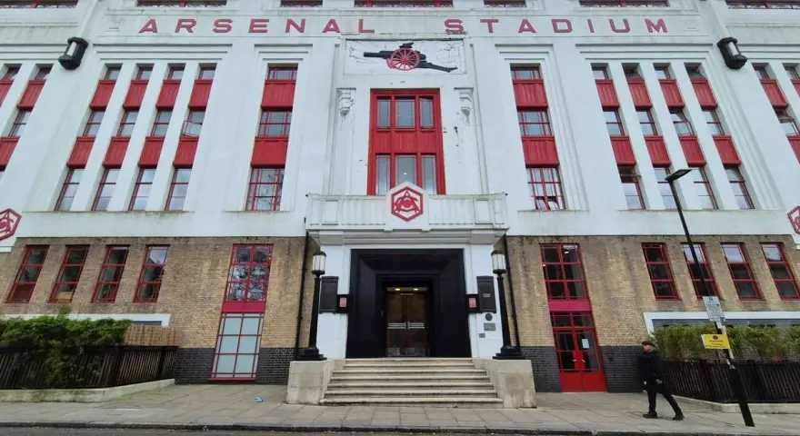 Dawny stadion Arsenalu w Highbury, z charakterystycznym napisem "ARSENAL STADIUM" i czerwonymi akcentami.