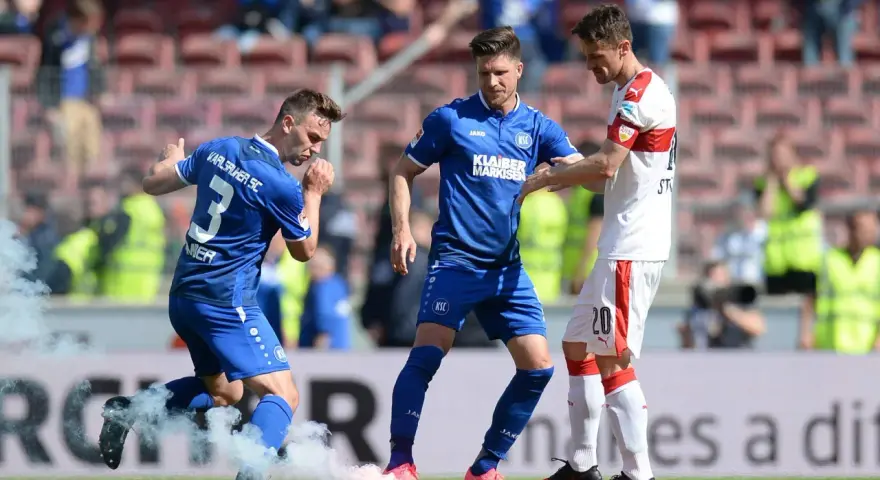 Piłkarze Karlsruher SC w niebieskich strojach, jeden z nich z numerem 3, otoczeni dymem z rac.