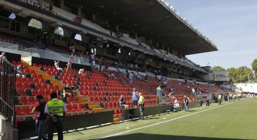 Puste trybuny stadionu Vallecas, z kilkoma osobami siedzącymi i stojącymi.