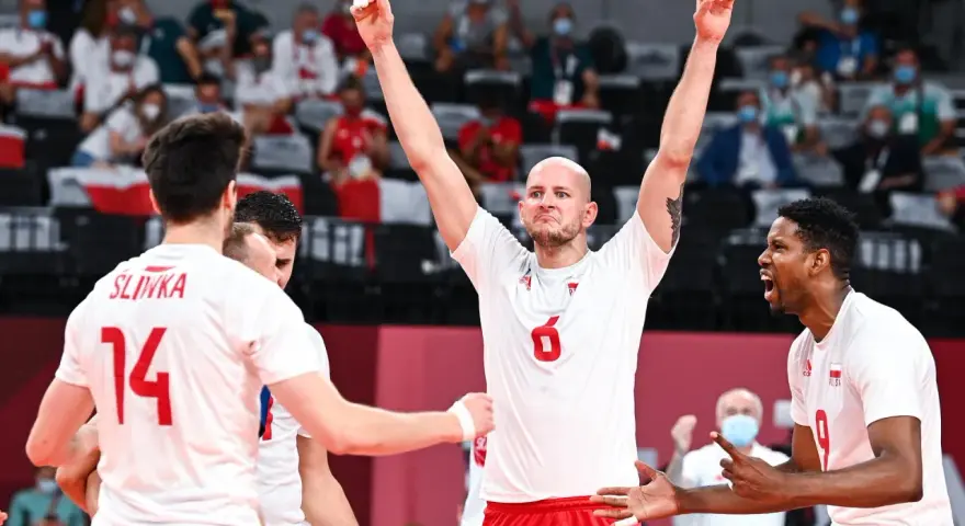 Siatkarze w białych strojach świętują zwycięstwo. Jeden z nich, z numerem 6, unosi ręce w geście triumfu. To kluczowy moment, być może decydujący o wygranej w piątym secie w meczu siatkarskim.