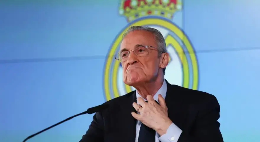 Florentino Pérez, prezes Realu Madryt, w garniturze, z ręką na szyi, na tle logo klubu.