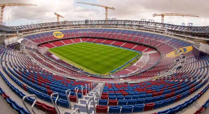 Stadion de la Cartuja w budowie, z widocznymi dźwigami i częściowo wykończonymi trybunami w kolorach czerwonym i niebieskim.