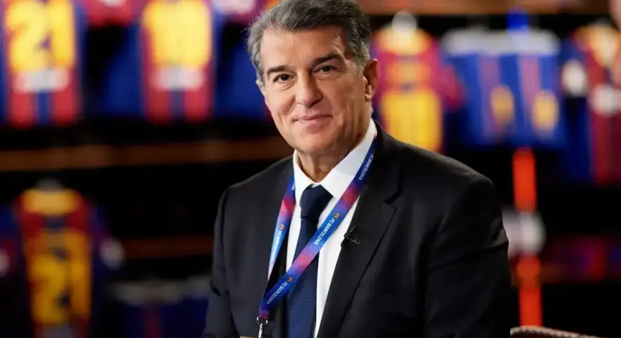 Uśmiechnięty prezes Barcelony, Joan Laporta, w garniturze, z identyfikatorem FC Barcelona na szyi.