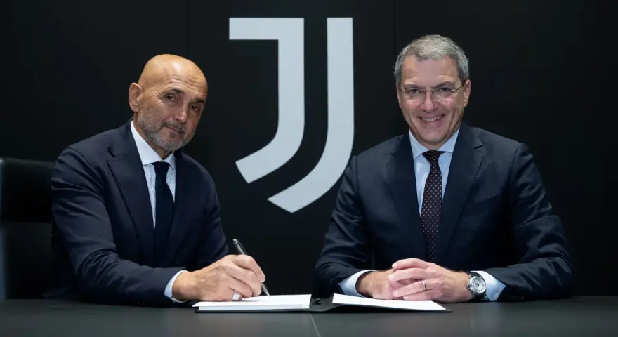 Dwóch mężczyzn w garniturach siedzi przy stole. Jeden z nich, łysy, podpisuje dokument. Za nimi logo Juventusu.