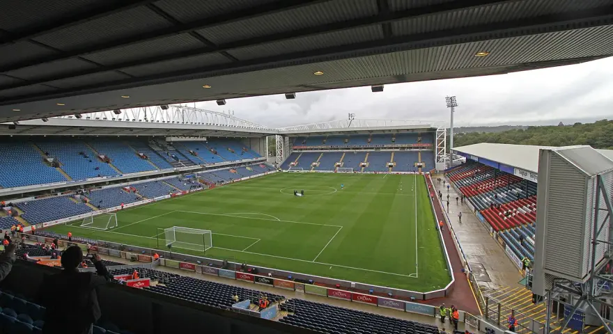 Widok na murawę i trybuny stadionu Ewood Park. Puste miejsca na niebieskich i czerwonych siedzeniach.