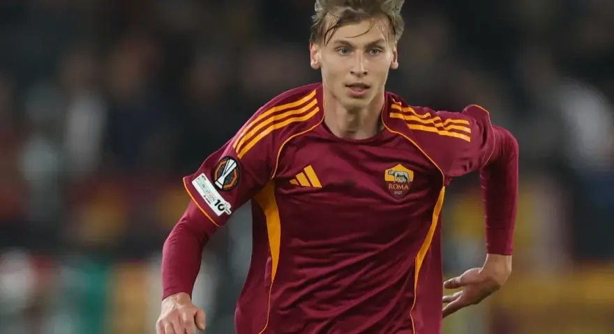 Piłkarz AS Roma w bordowej koszulce z żółtymi pasami, gotowy do gry przeciwko Genoa CFC.