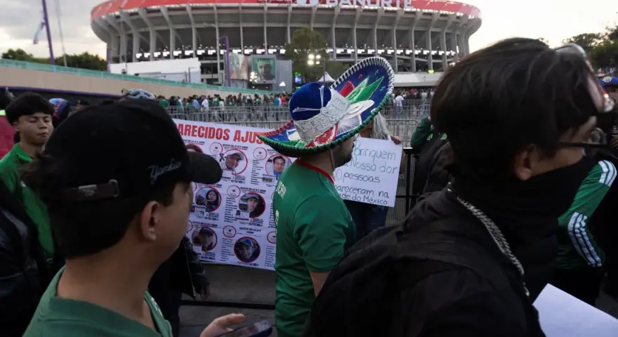 Tłum ludzi przed stadionem Azteca. Na pierwszym planie mężczyzna w meksykańskim kapeluszu, obok baner z portretami zaginionych.