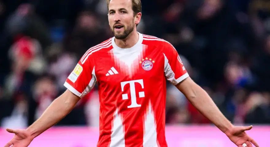 Piłkarz Harry Kane w czerwonej koszulce Bayernu Monachium, zastanawia się, ile zarabia.