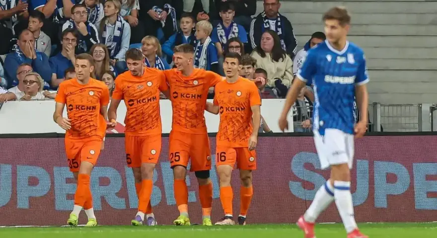 Piłkarze Zagłębia Lubin w pomarańczowych strojach świętują bramkę, podczas gdy zawodnik Lecha Poznań w niebieskim oddala się.