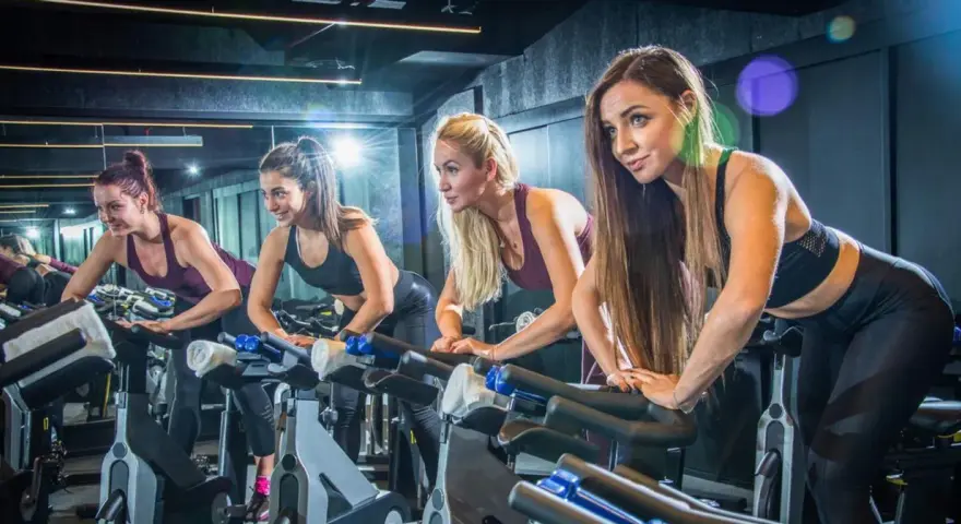 Cztery kobiety ćwiczą na rowerach stacjonarnych. Ile powinien trwać trening cardio? To zależy od celów, ale często 30-60 minut to dobry punkt wyjścia.