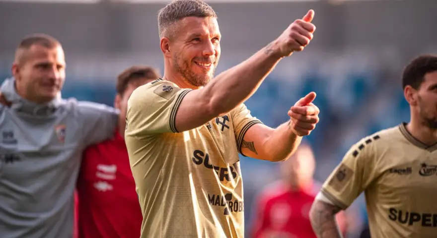 Uśmiechnięty Lukas Podolski pokazuje kciuk w górę, jakby podsumowywał swoje świetne statystyki.