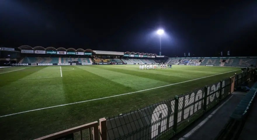 Piłkarze na murawie stadionu Górnik Łęczna, oświetlonego jupiterami.