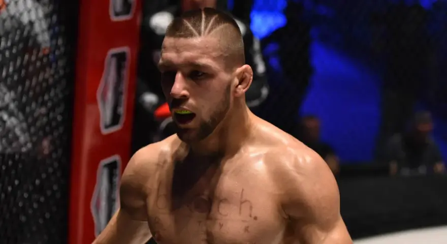 Zacięty zawodnik MMA z charakterystyczną fryzurą i ochraniaczem na zęby, gotowy do walki.