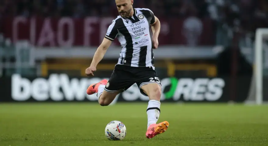 Piłkarz Jesper Karlström w czarno-białej koszulce Udinese Calcio kopie piłkę na zielonej murawie stadionu.